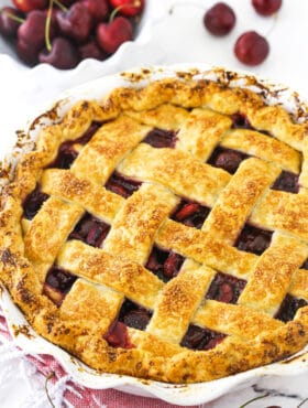 A cherry pie inside of a 9-inch pie dish with a bowl of sweet cherries in the background