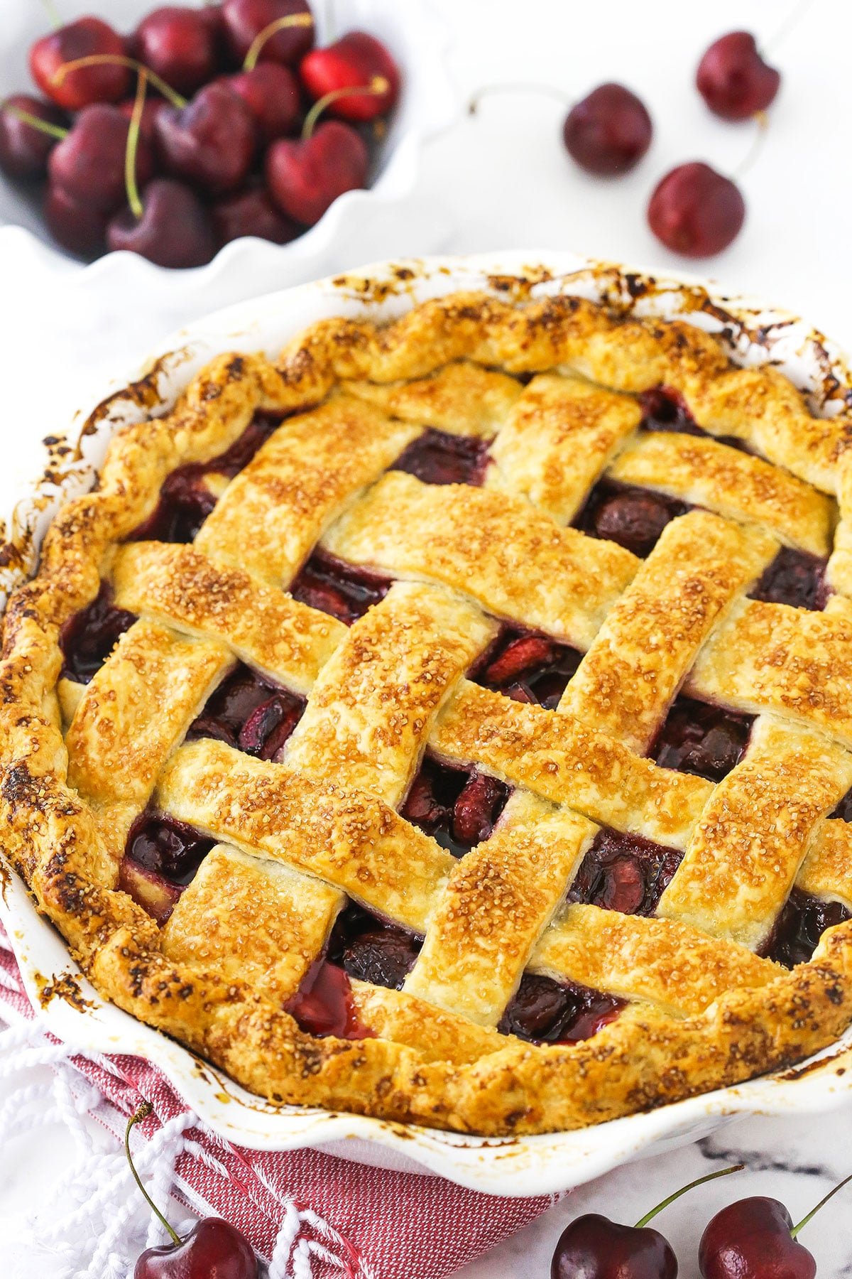 A cherry pie inside of a 9-inch pie dish with a bowl of sweet cherries in the background