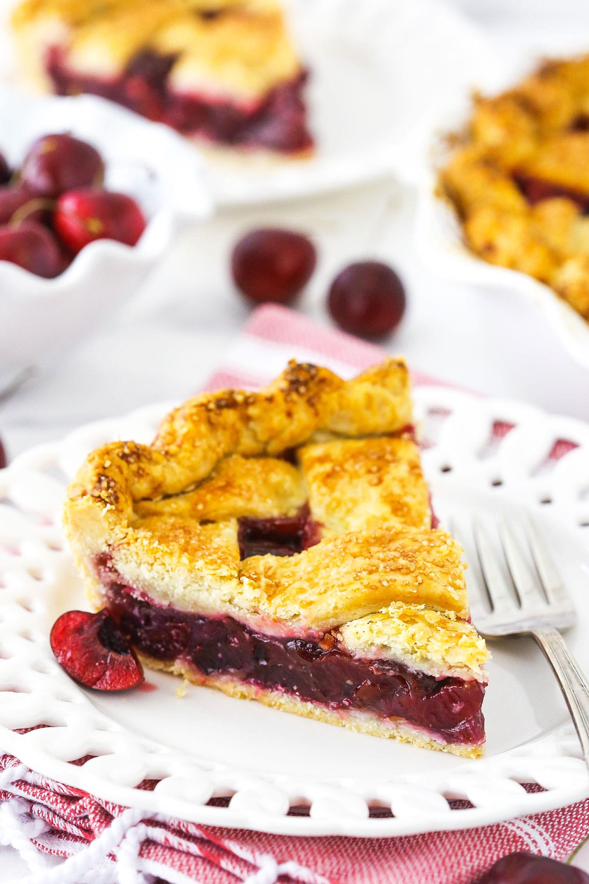 A piece of cherry pie on a dessert plate with a metal fork beside it