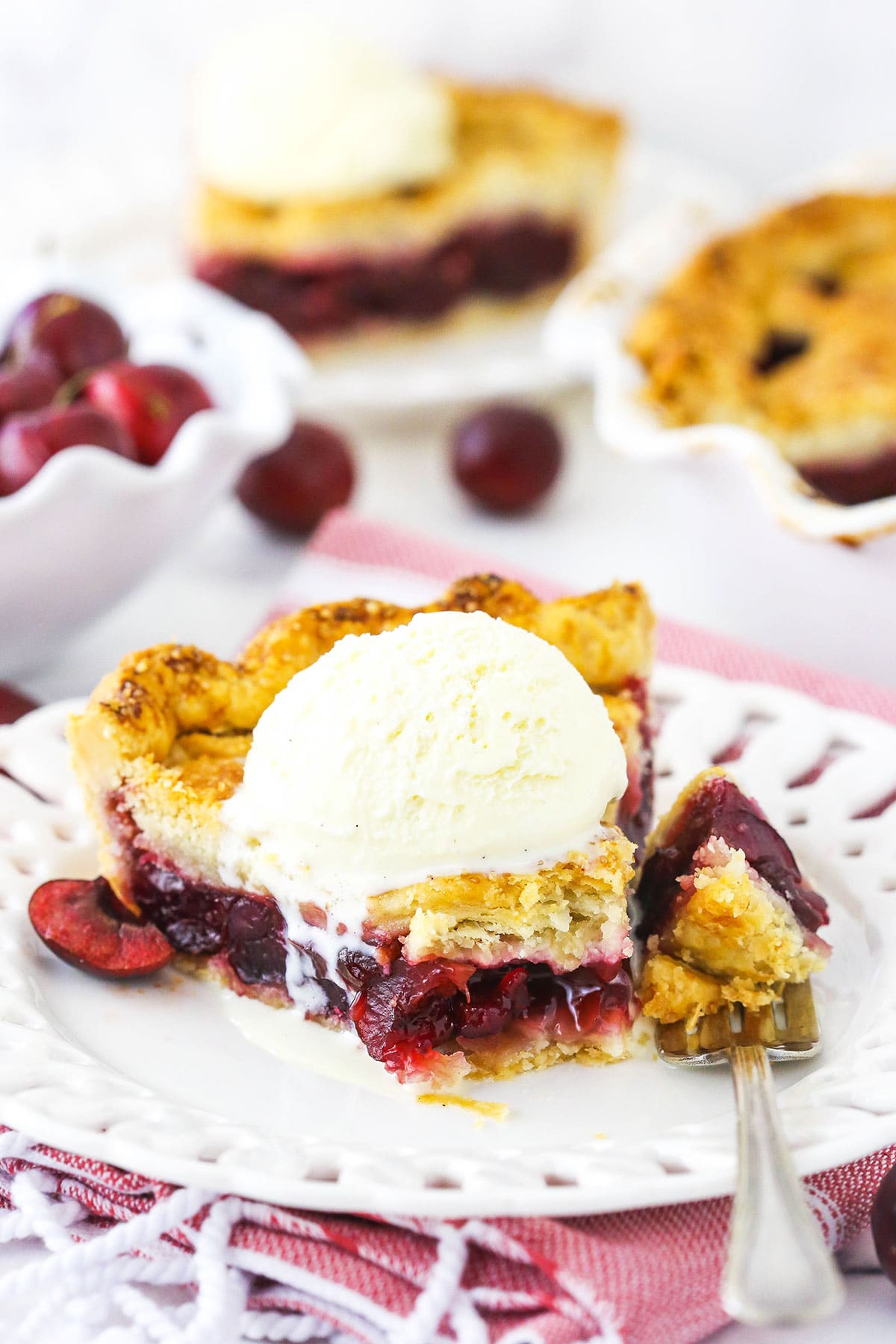 A slice of cherry pie on a plate with one bite on a fork