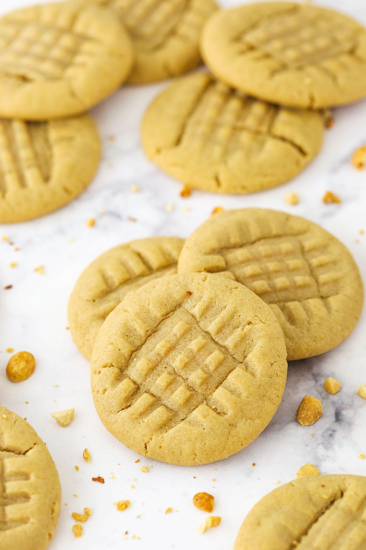 A group of three peanut butter cookies on a marble countertop with more cookies surrounding them