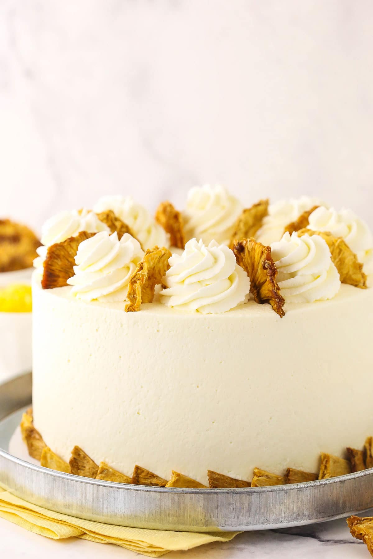 A pineapple layer cake topped with swirls of whipped cream frosting and dried pineapple pieces