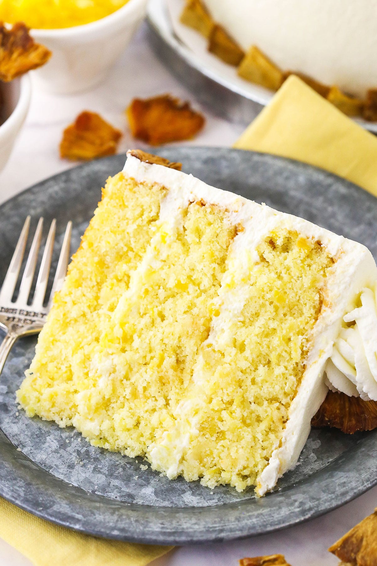 A slice of pineapple layer cake on a plate with the remaining cake behind it