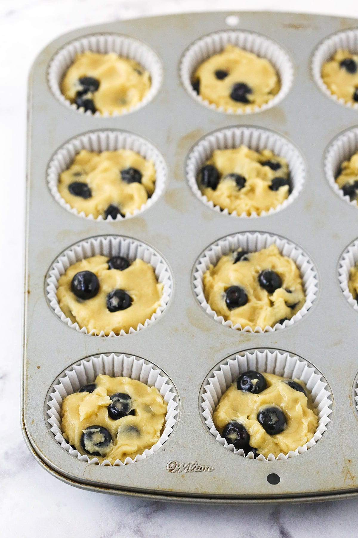 Blueberry muffin batter inside the cups of a large muffin tin