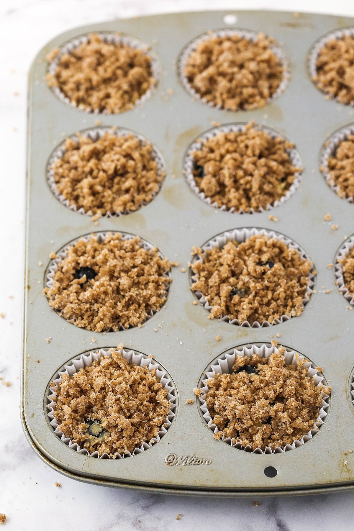 A twelve-count muffin tin containing liners, batter and streusel