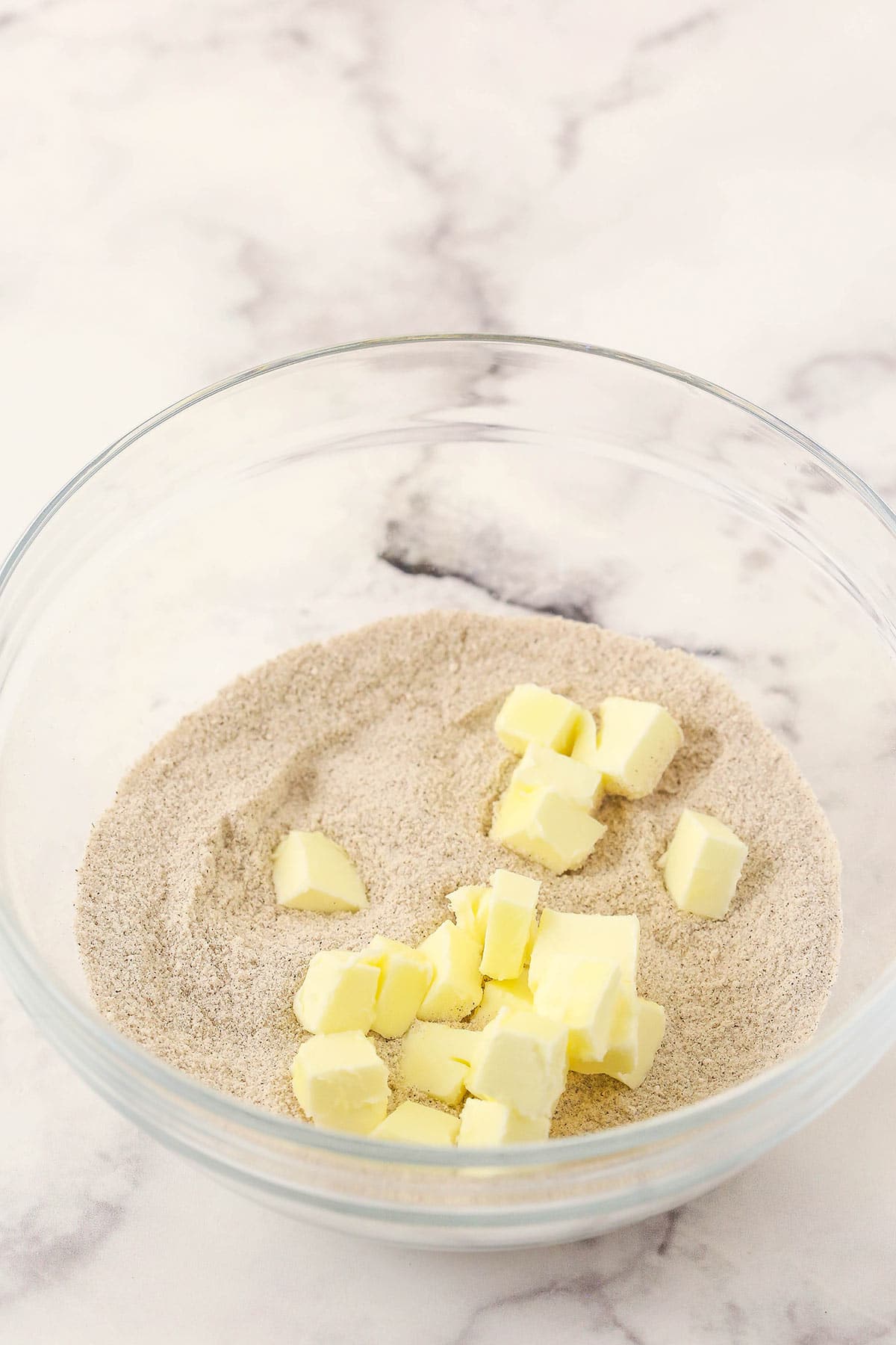 The combined dry ingredients for the streusel in a bowl with cubes of cold butter on top