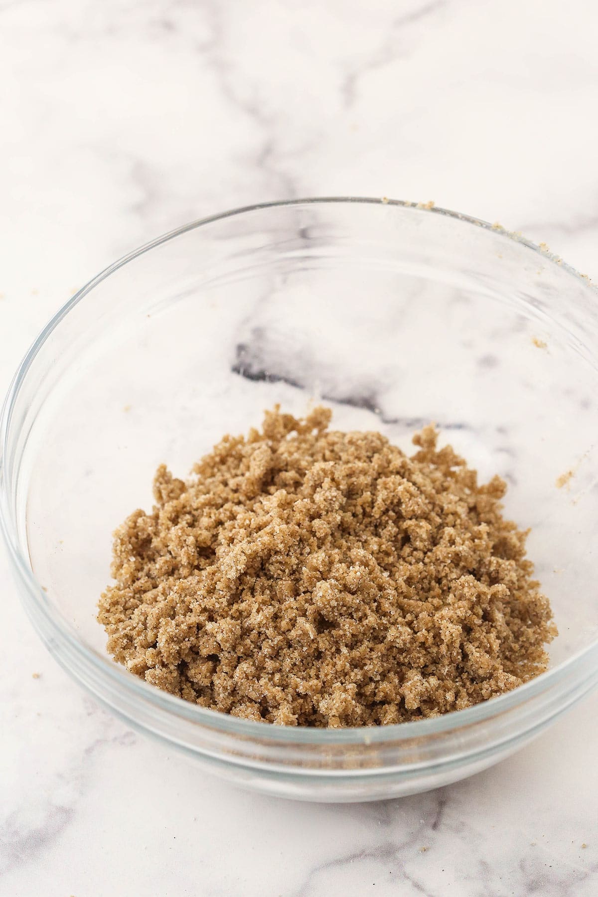 A homemade cinnamon streusel topping inside of a clear bowl on a kitchen countertop