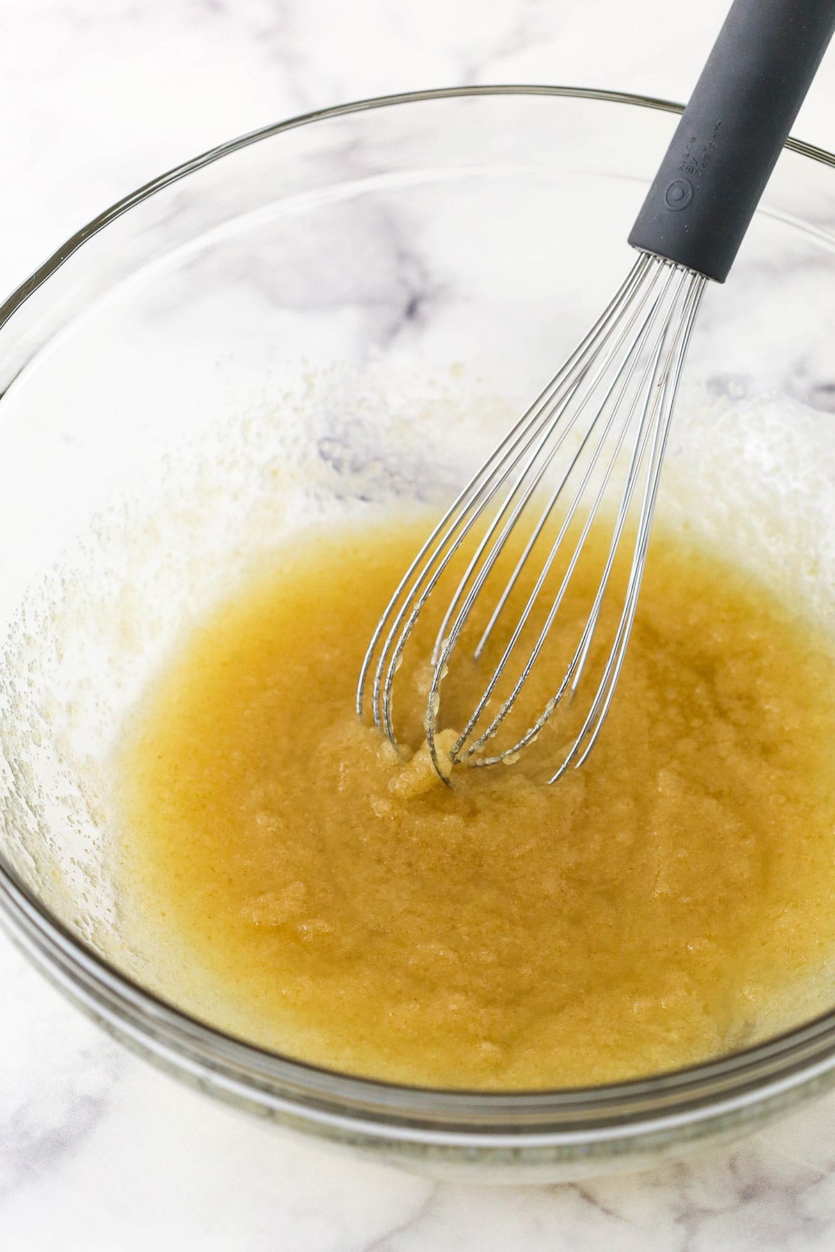 A mixture of vegetable oil, melted butter, brown sugar and granulated sugar inside of a large glass bowl