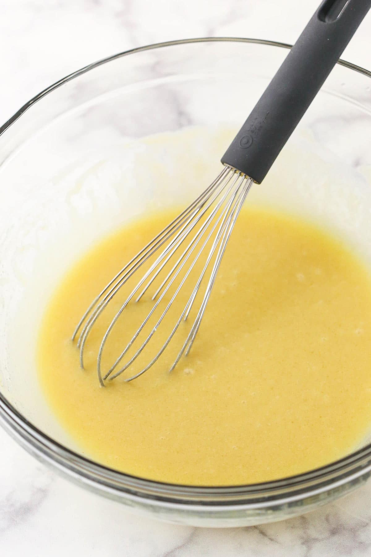 The combined wet ingredients inside of a glass mixing bowl with a metal whisk