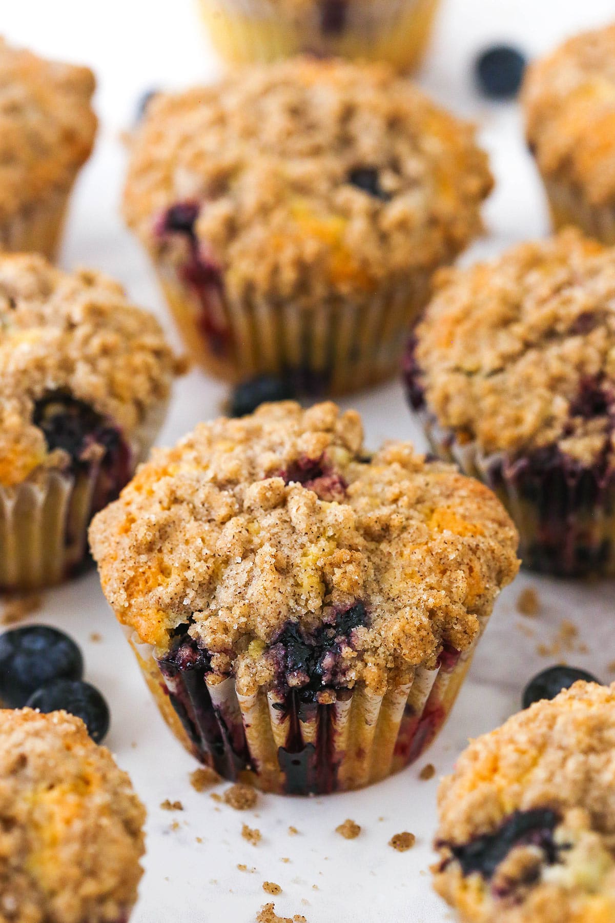 A bunch of blueberry muffins on a granite countertop with a few fresh blueberries