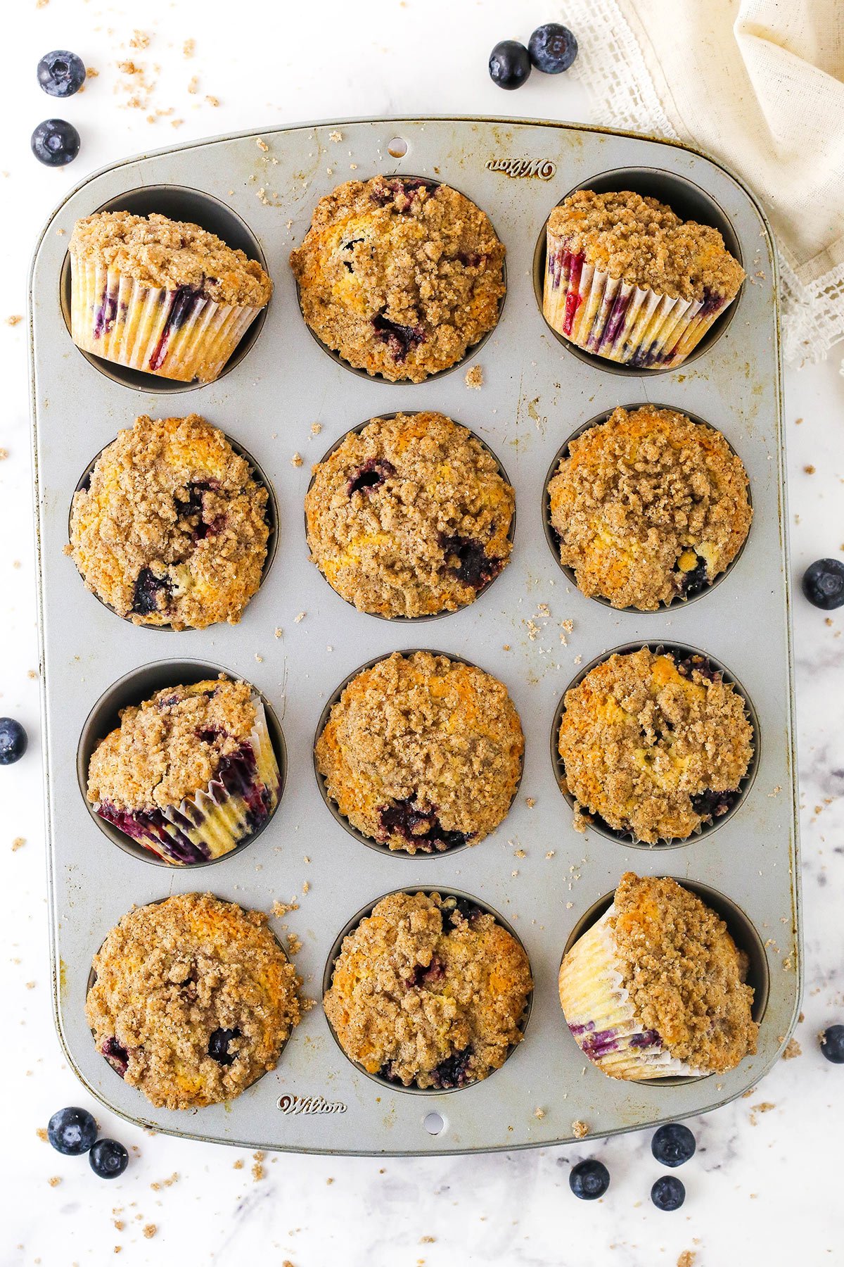 A 12-count muffin tin with a homemade blueberry muffin inside of each muffin cup
