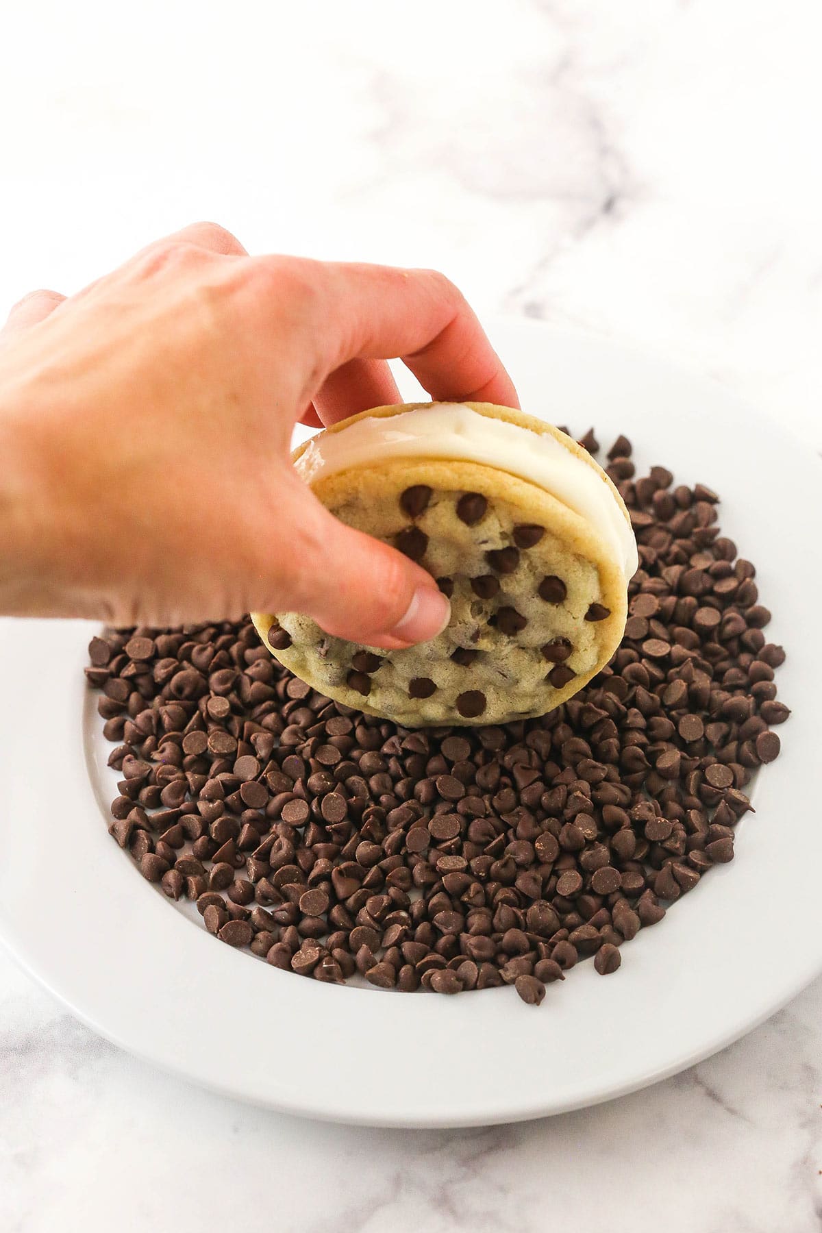 A chocolate chip cookie sandwich being rolled onto a plate of mini chocolate chips