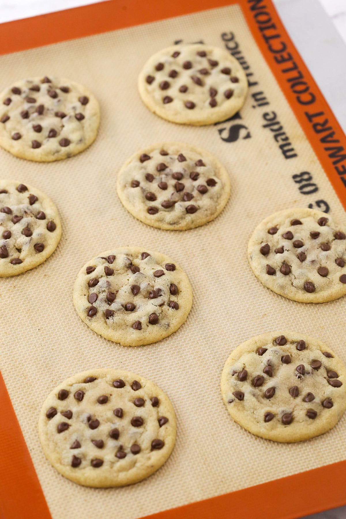 Eight homemade chocolate chip cookies on a baking sheet lined with a Silpat baking mat