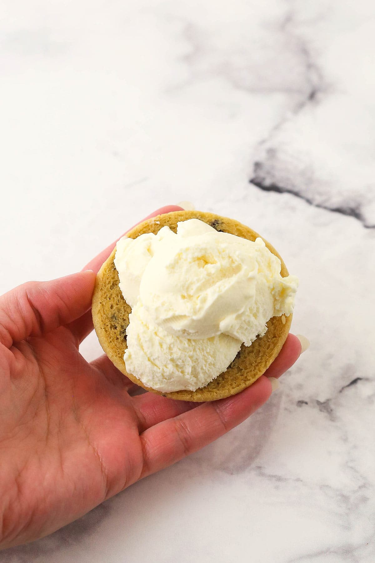 A scoop of vanilla ice cream on the bottom end of a cooled chocolate chip cookie