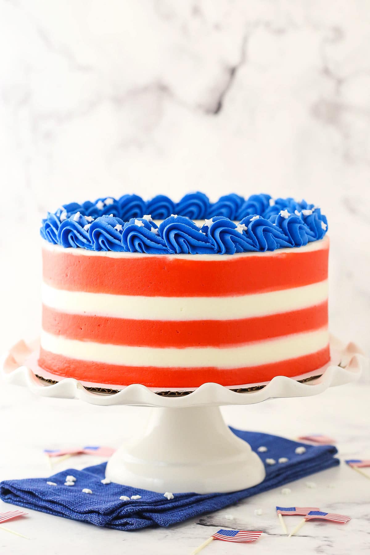 A tall cake stand holding a 4th of July marble cake with small American flag toothpicks on the counter beneath it