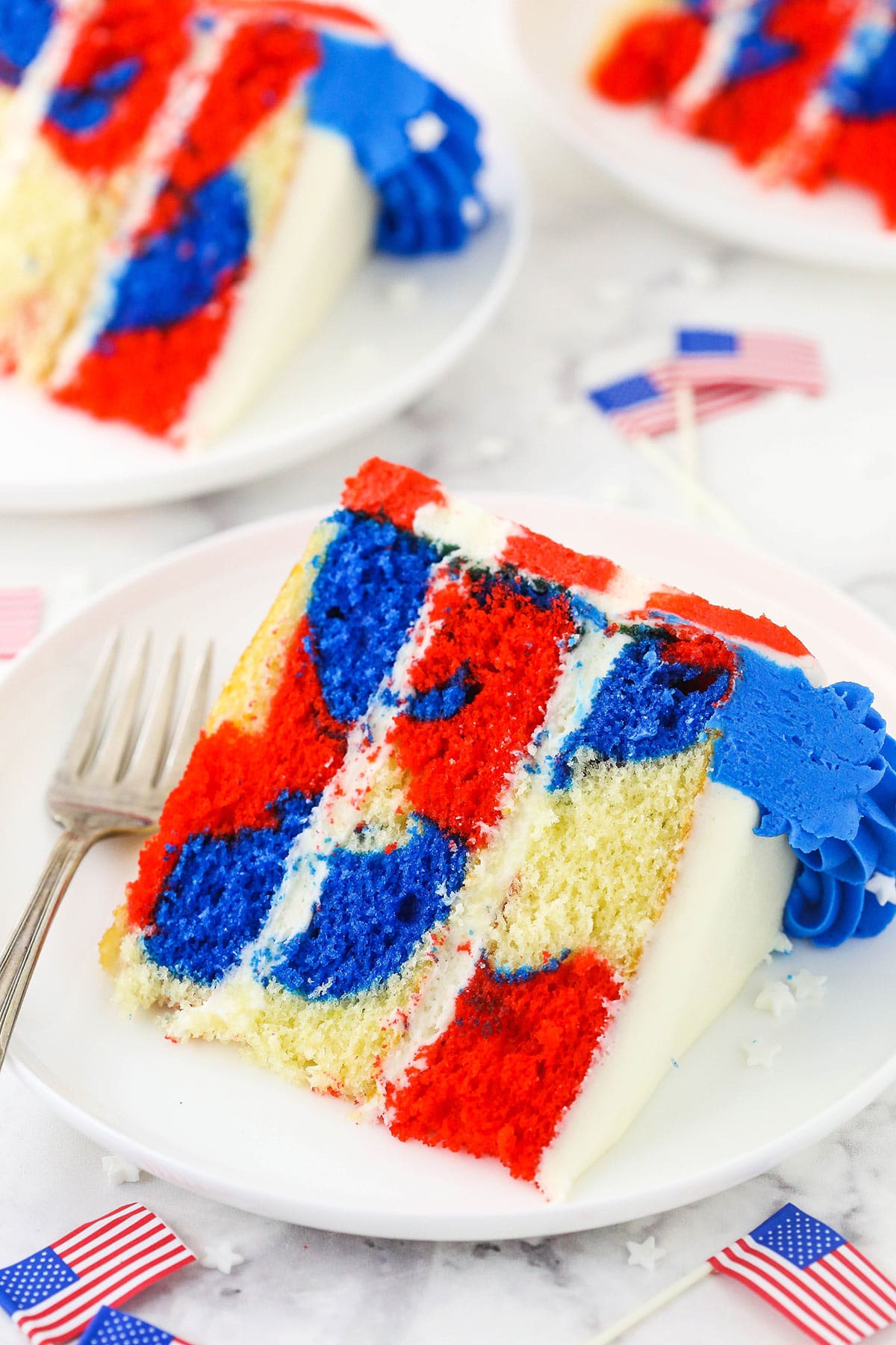 A piece of July 4th cake on a plate with two more slices behind it