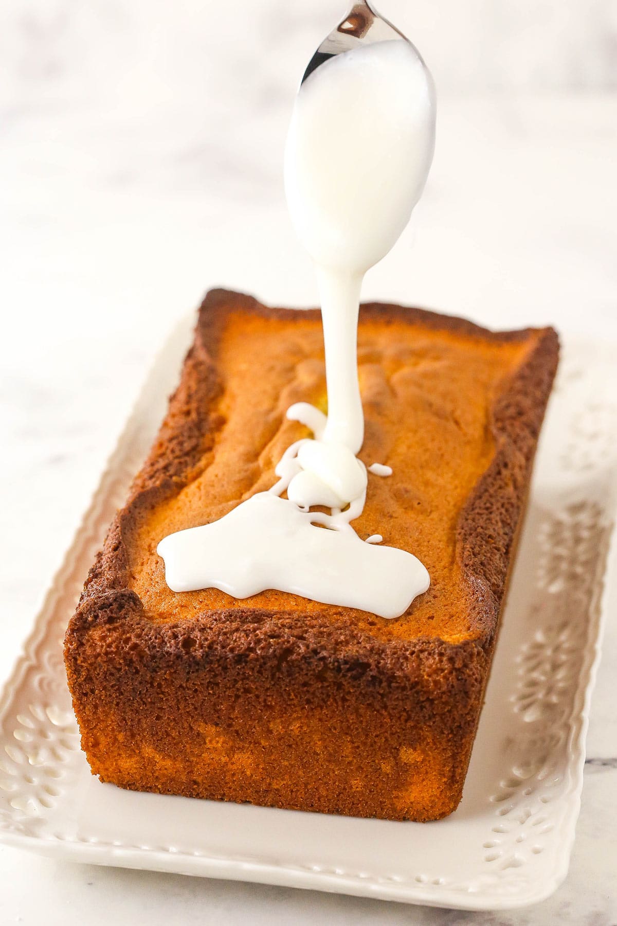 A spoon drizzling some homemade glaze onto a cooled breakfast cake