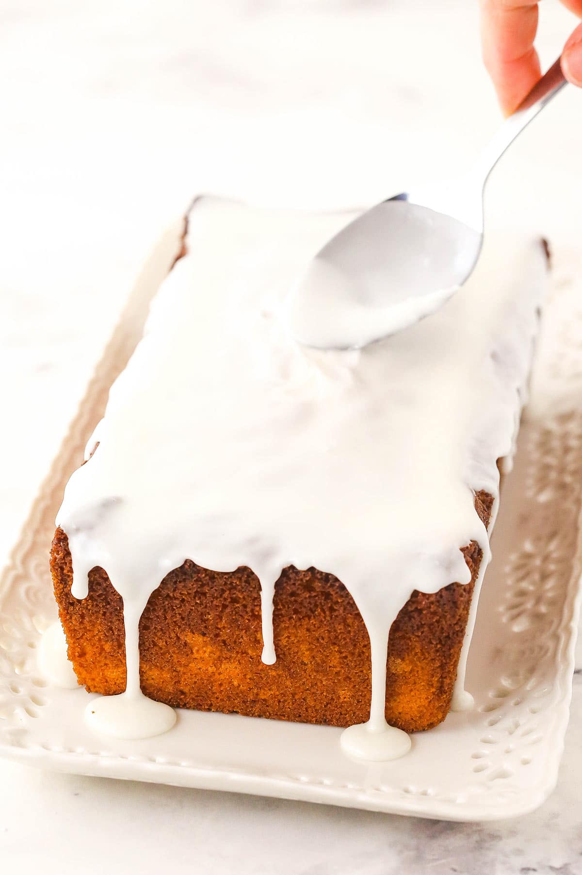 Homemade lemon icing being spread onto a cooled lemon loaf cake