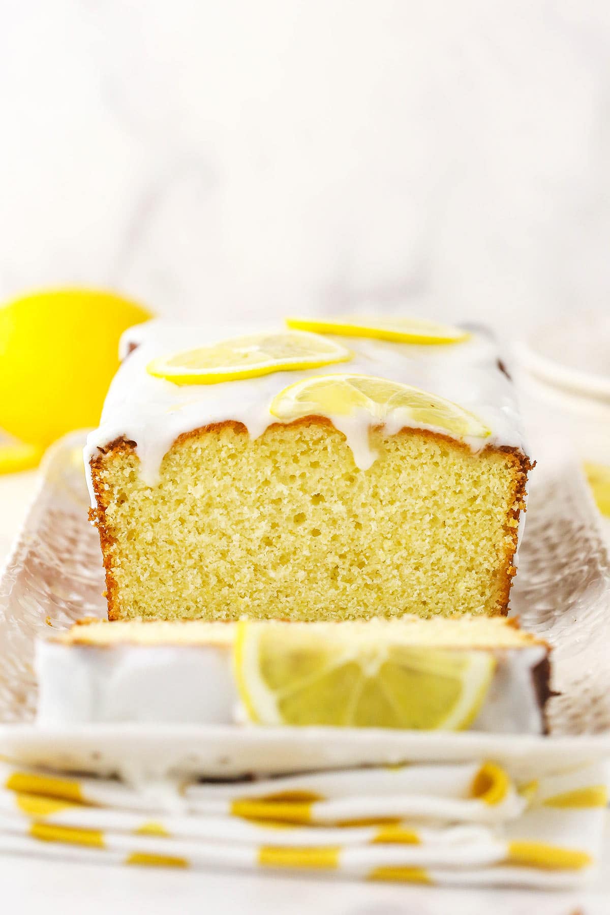 A lemon loaf on a long platter with a white and yellow kitchen towel underneath it