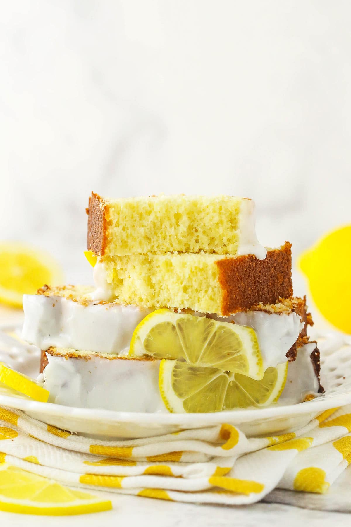 Slices of lemon loaf cake piled onto a plate with a fresh lemon beside it