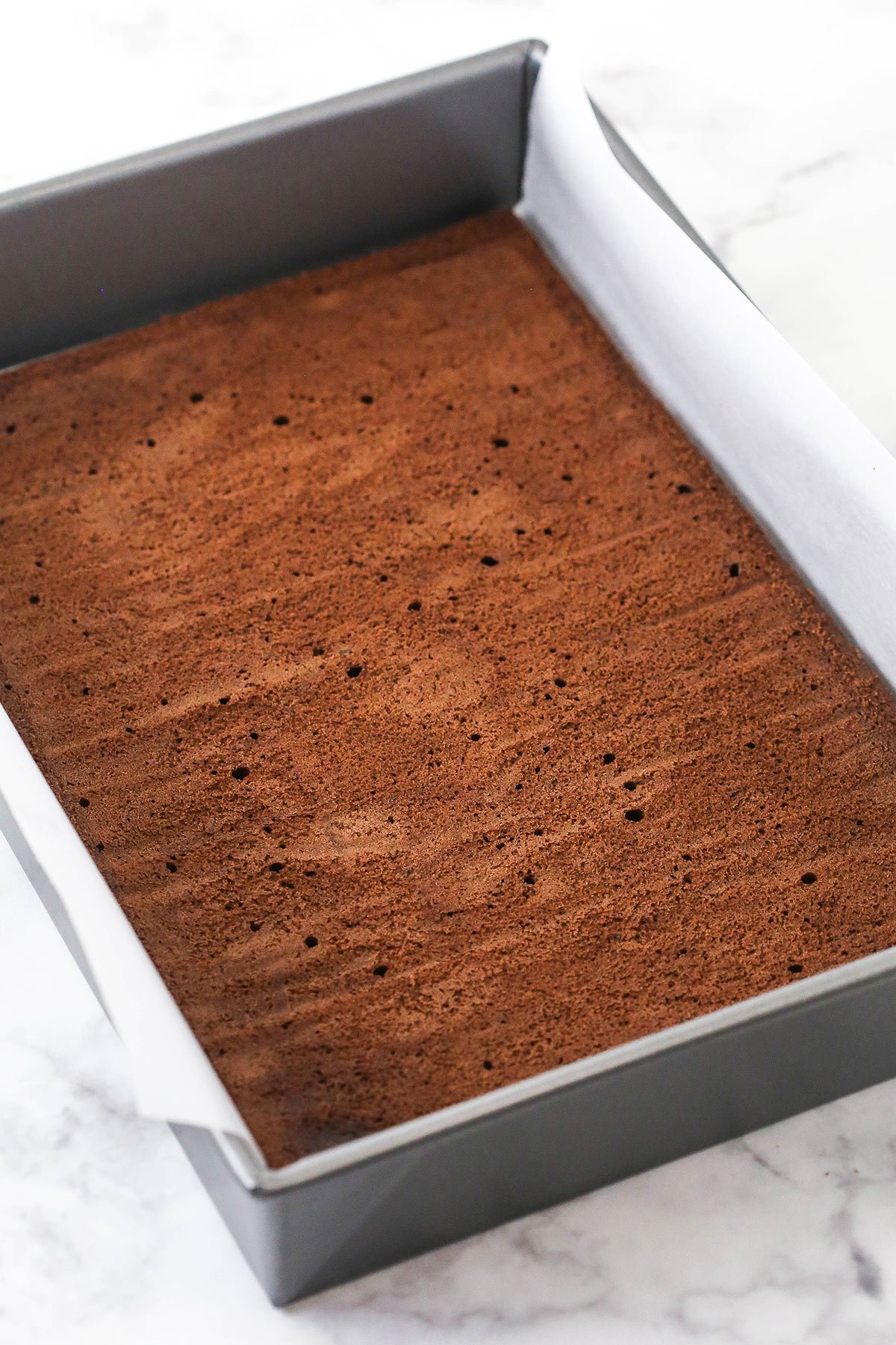 The bottom cookie base inside of a pan lined with enough parchment paper to extend up either side of the pan