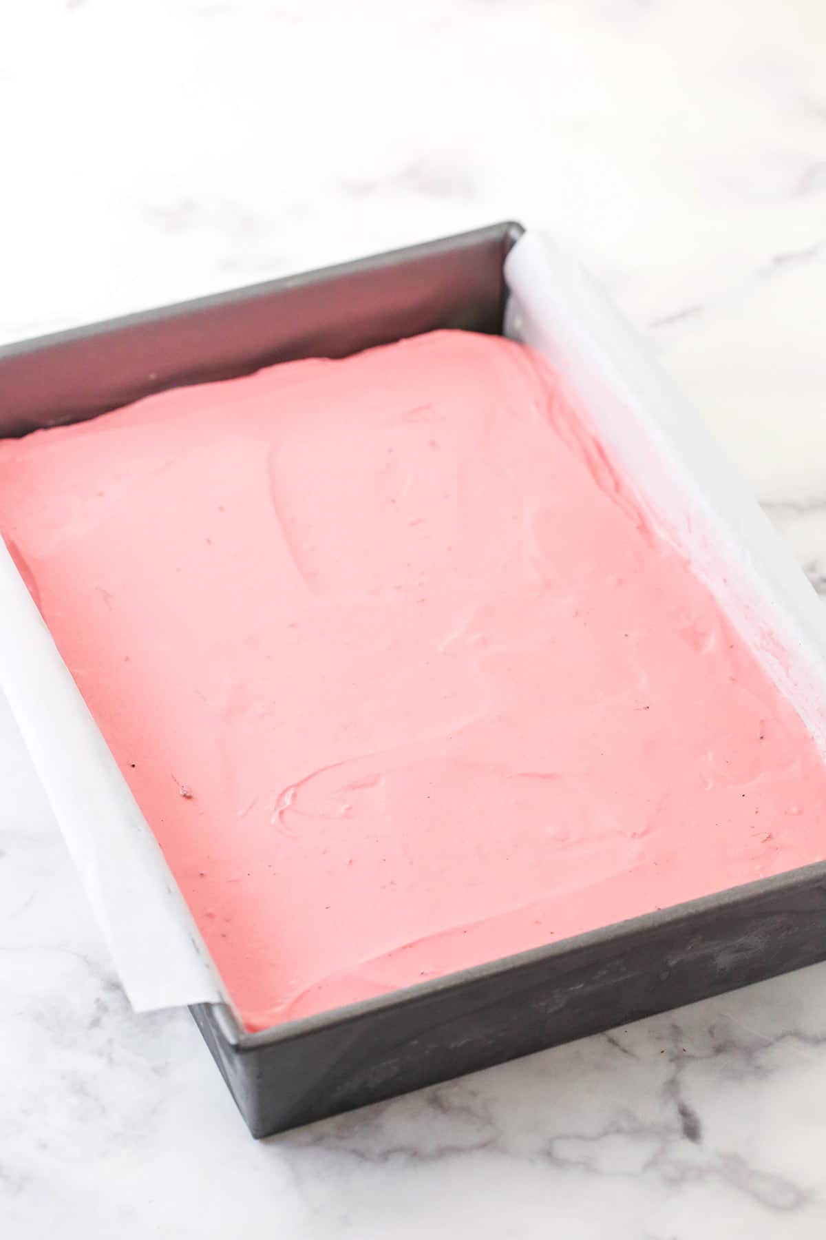 The strawberry ice cream layer on top of the vanilla ice cream layer on top of the bottom cookie base in a pan