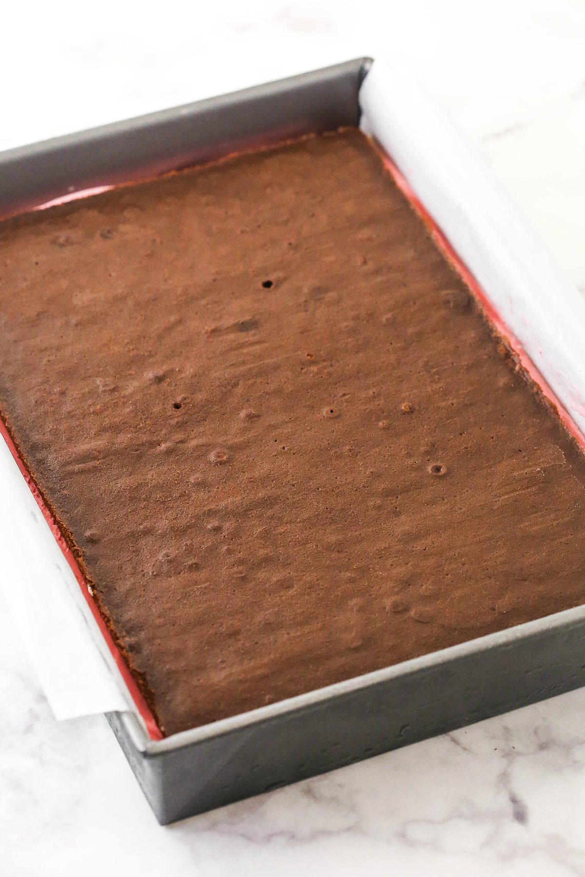 An assembled batch of ice cream sandwiches inside of a pan lined with overhanging parchment paper