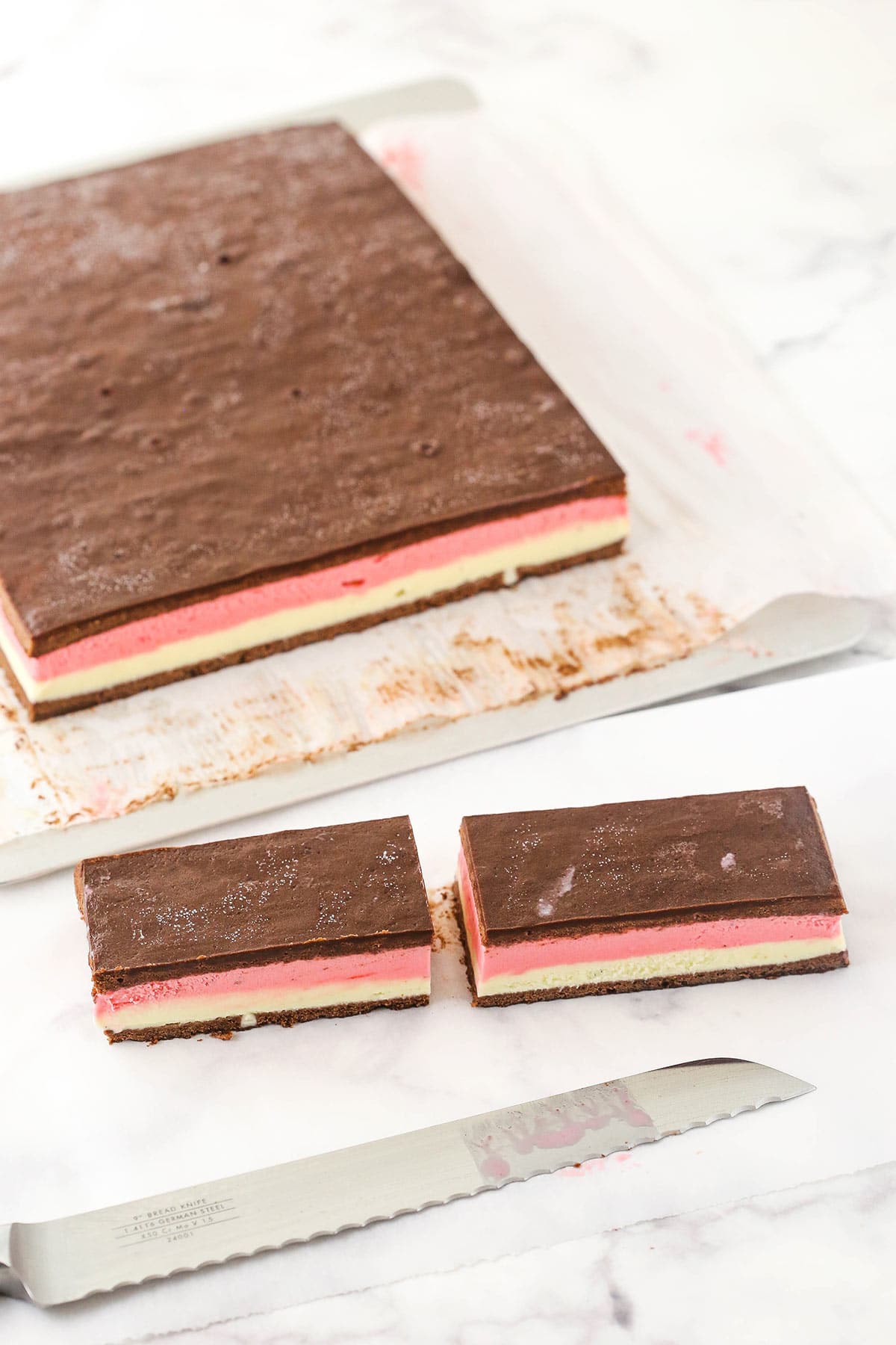 A batch of Neapolitan ice cream sandwiches on a lined pan with two rectangles cut off and a sharp knife beside them
