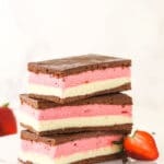 A stack of three Neapolitan ice cream sandwiches on a plate with a halved strawberry leaning against the stack
