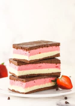 A stack of three Neapolitan ice cream sandwiches on a plate with a halved strawberry leaning against the stack