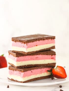 A stack of three Neapolitan ice cream sandwiches on a plate with a halved strawberry leaning against the stack