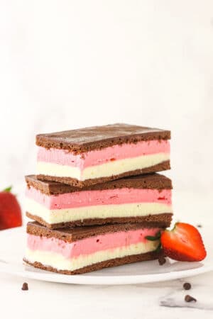 A stack of three Neapolitan ice cream sandwiches on a plate with a halved strawberry leaning against the stack