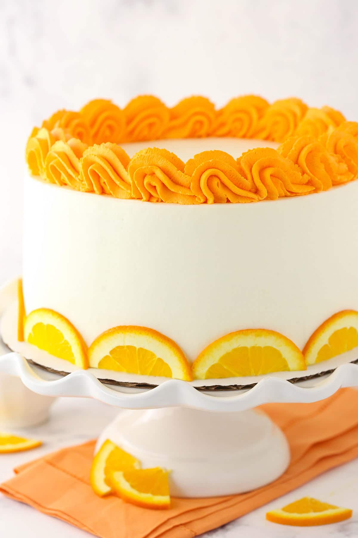 A citrus layer cake with whipped cream cheese frosting on a tall cake stand