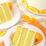 A slice of cake on a plate with a fork and a bowl of orange slices in the background