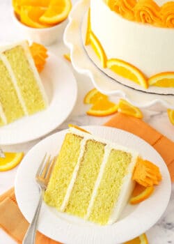 A slice of cake on a plate with a fork and a bowl of orange slices in the background
