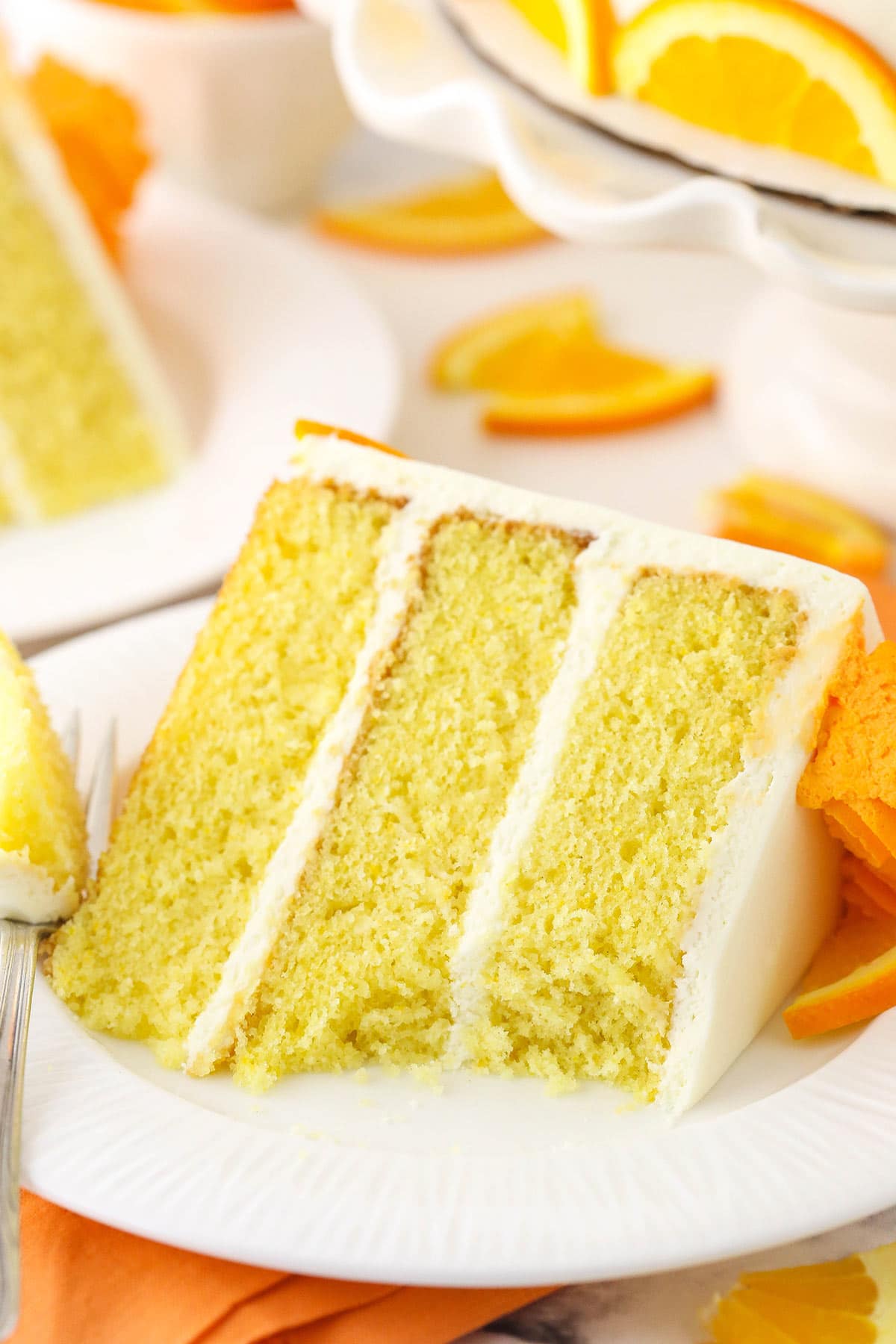 A slice of orange layer cake on a dessert plate with one bite on a fork
