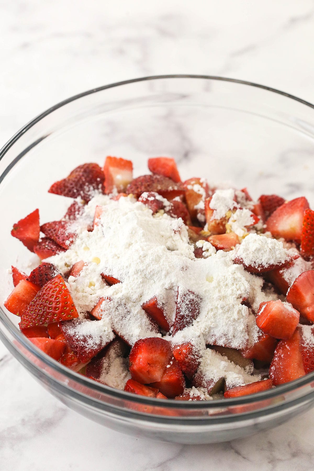 Chopped strawberries and rhubarb in a glass bowl with flour, sugar, orange juice, vanilla extract salt added on top