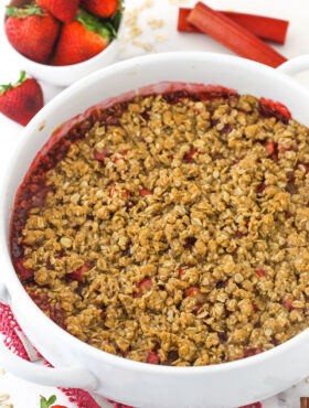 Baked strawberry rhubarb crisp in a round white baking dish with bowl of strawberries in background