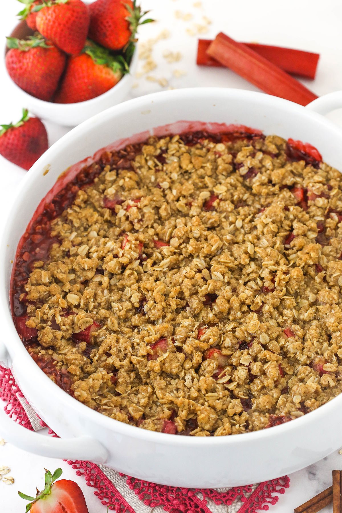 Baked strawberry rhubarb crisp in a round white baking dish with bowl of strawberries in background