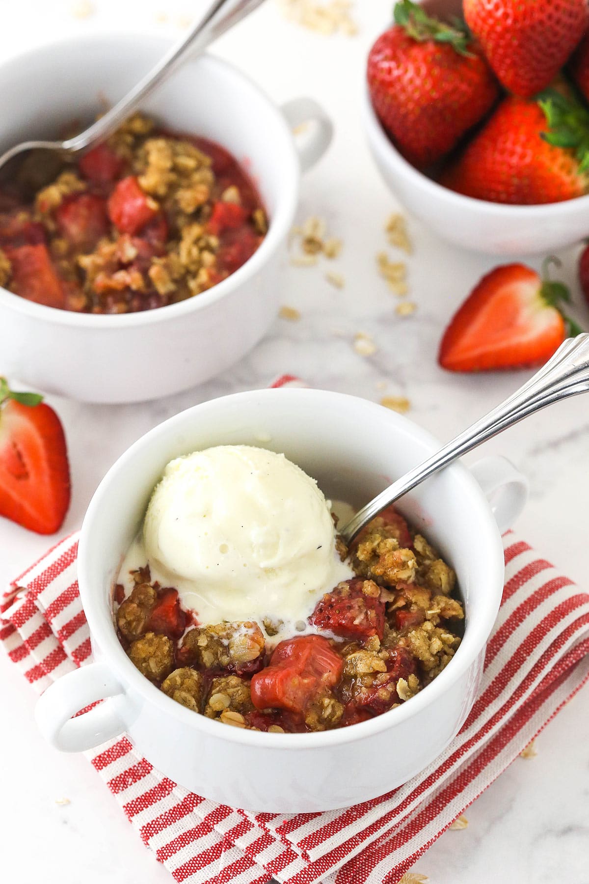 strawberry rhubarb crisp with a scoop of ice cream on top on a red and white striped napkin