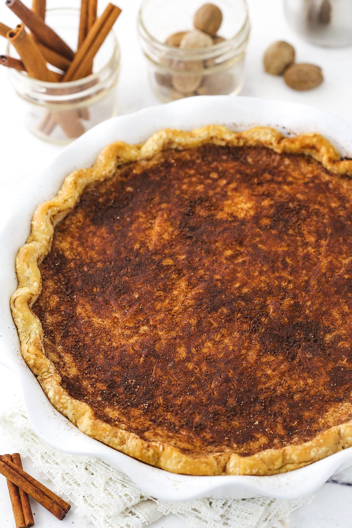 A sugar cream pie in a pie dish with a jar of cinnamon sticks behind it