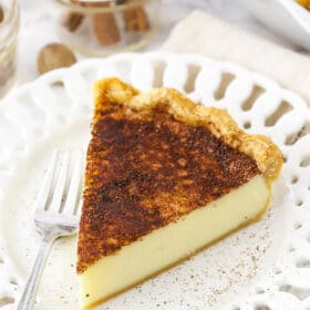 A slice of sugar cream pie on a white plate with a metal fork beside it