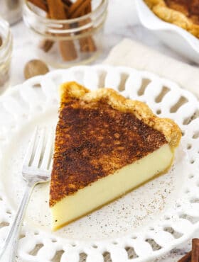 A slice of sugar cream pie on a white plate with a metal fork beside it