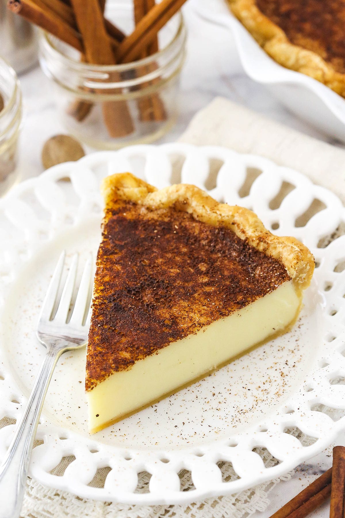 A slice of sugar cream pie on a white plate with a metal fork beside it