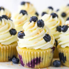 A batch of homemade cupcakes on a plastic cake stand with a wooden base