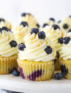 A batch of homemade cupcakes on a plastic cake stand with a wooden base