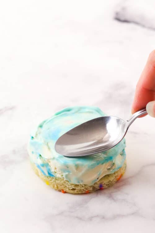 A metal spoon being used to spread ice cream onto a circle of cake