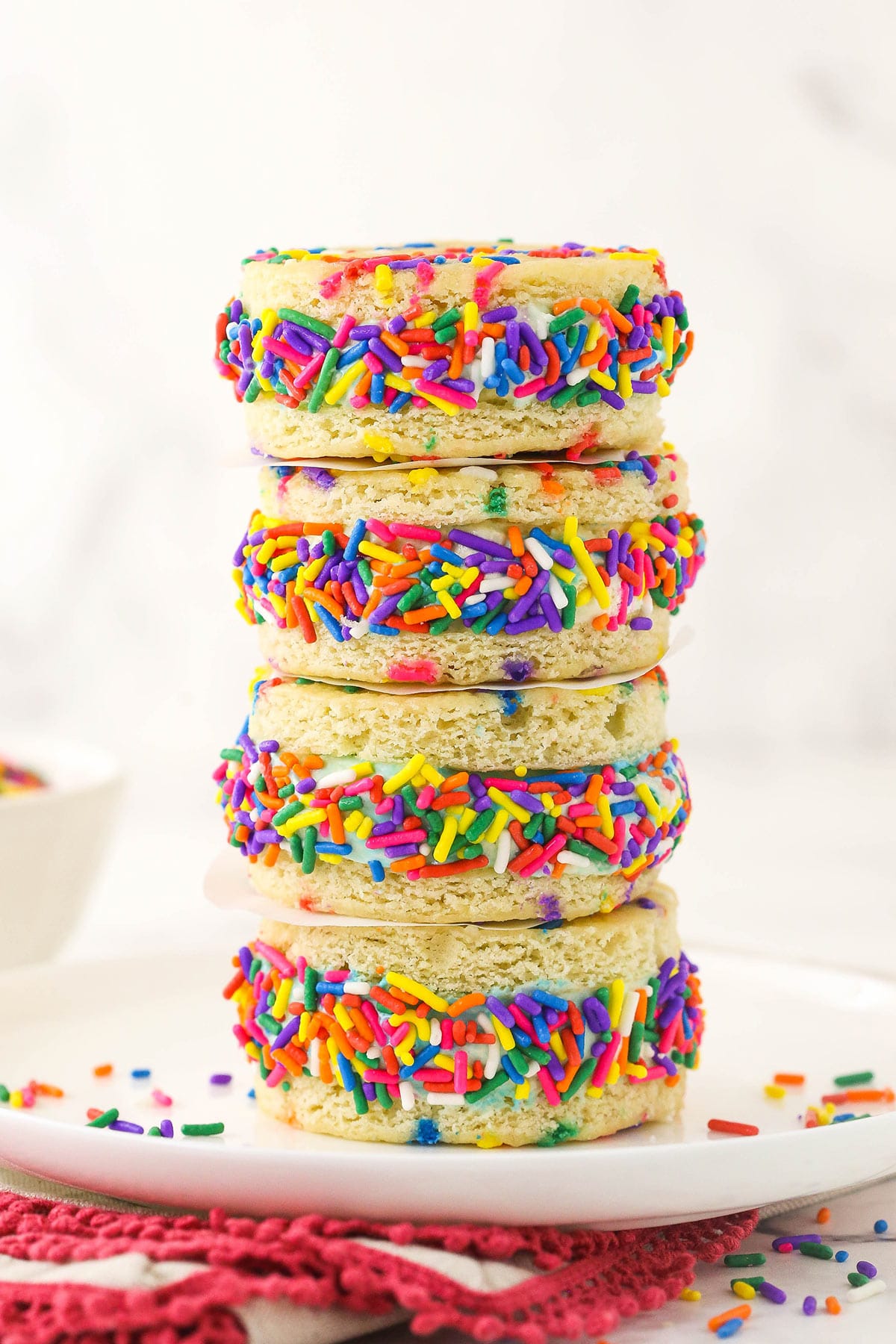 Two circles of confetti cake are separated by a sprinkle-studded layer of cake batter ice cream in these show-stopping ice cream sandwiches! A stack of four cake batter ice cream sandwiches on a dessert plate