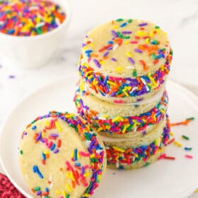 A stack of three ice cream sandwiches with another one beside them and a bowl of sprinkles in the background
