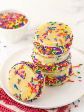 A stack of three ice cream sandwiches with another one beside them and a bowl of sprinkles in the background
